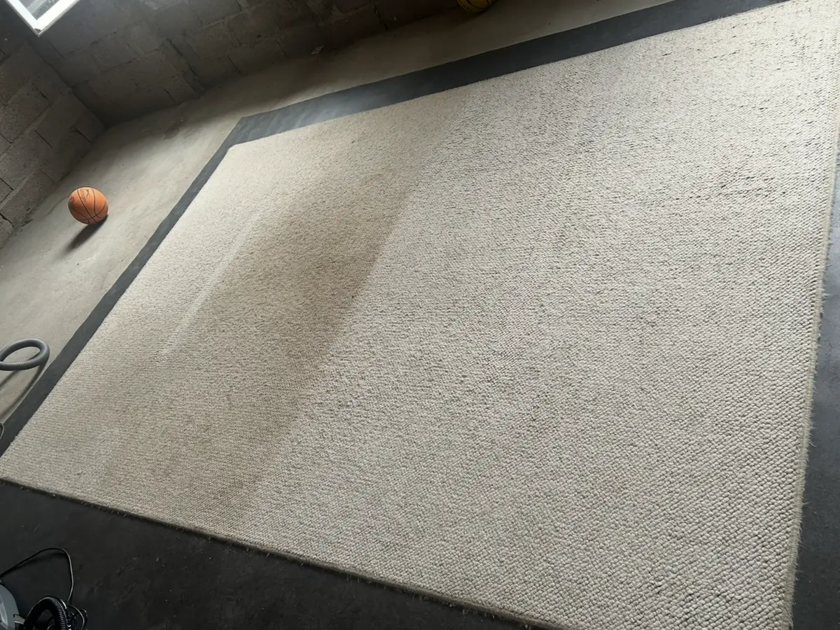 Grand tapis en laine en cours de nettoyage, bande grise pas encore traitée à côté de la partie propre